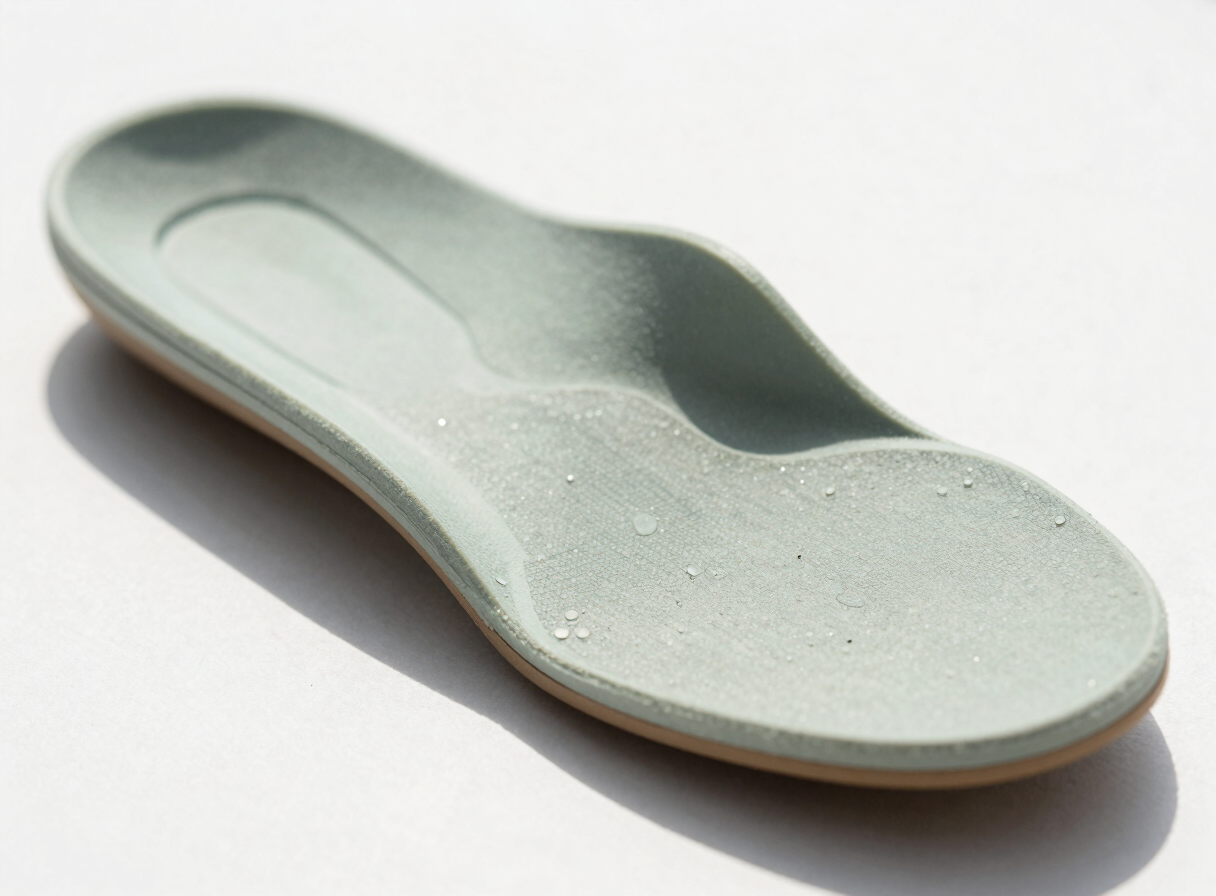 Macro shot of a custom-molded orthotic insole showing structural support layers, bright natural daylight, soft sage tones, 35mm